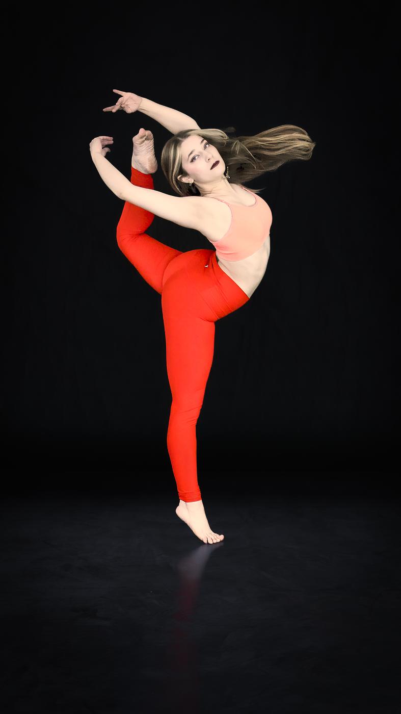 Ariella Sinclair in a dance kick pose in red leggings against a black backdrop