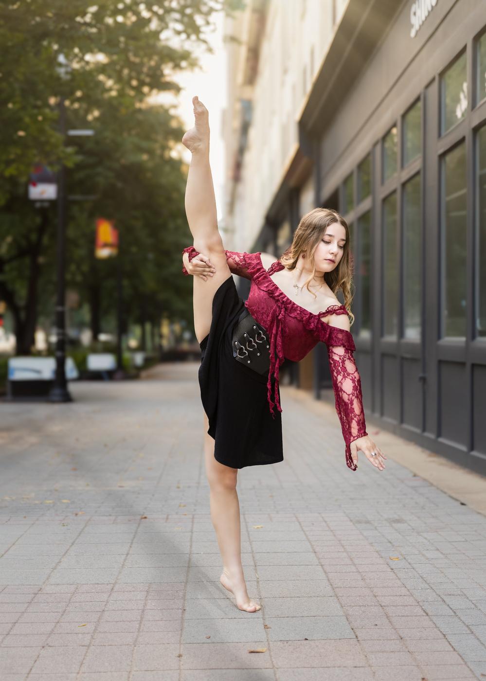 Ariella Sinclair performing a high leg extension in burgundy lace on the street