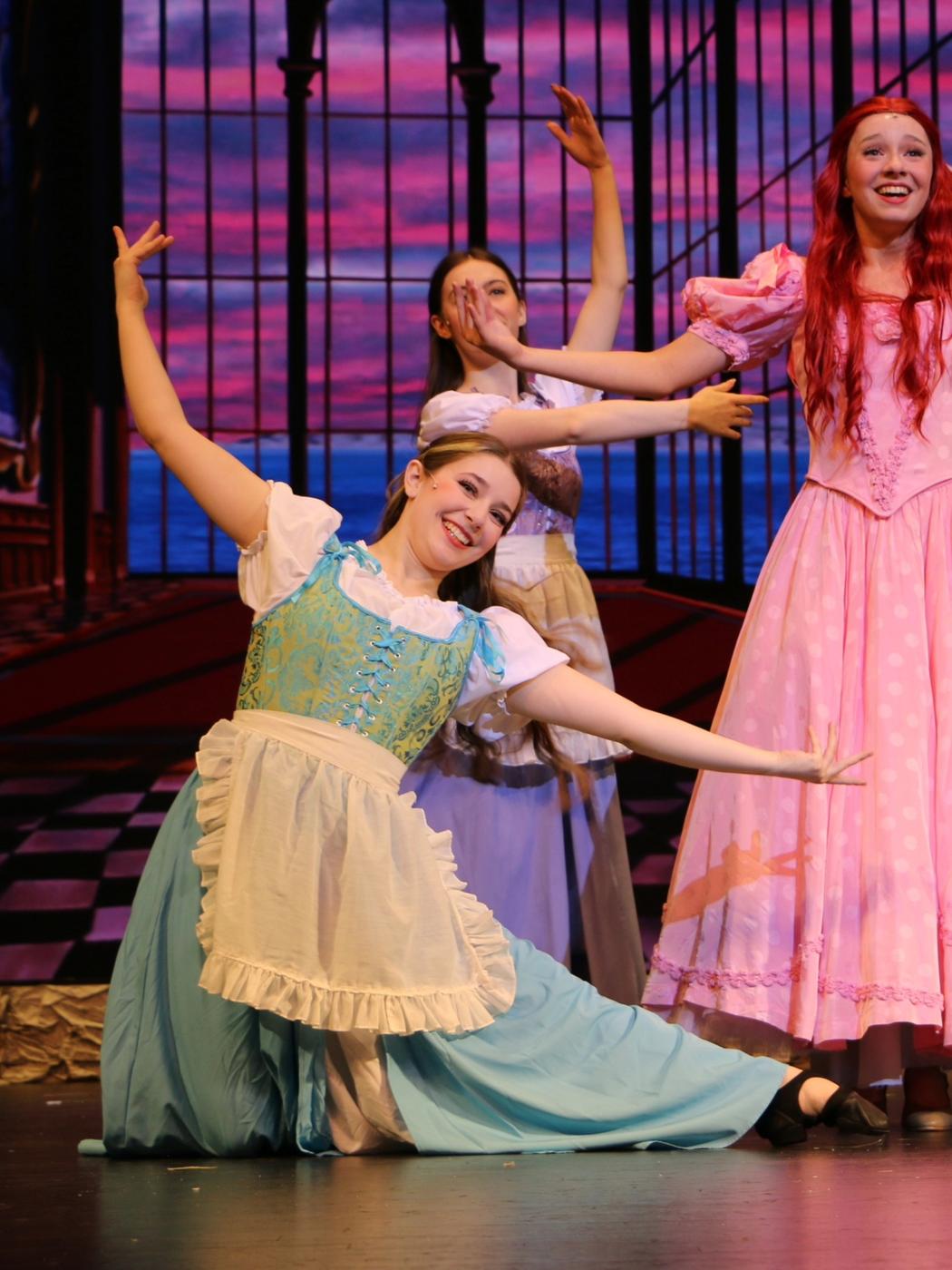 Ariella Sinclair as a maid in The Little Mermaid with cast members in pink gowns behind
